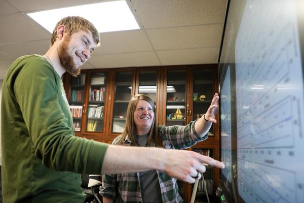 Student and a staff member looking at graphs on a smartboard